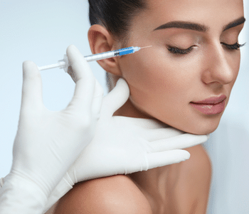 A person with closed eyes receives a cosmetic injection in the face near the cheekbone from a gloved medical professional, suggesting a beauty or skincare procedure. Bella Lei Aesthetics and Wellness - Flemming Island, Florida